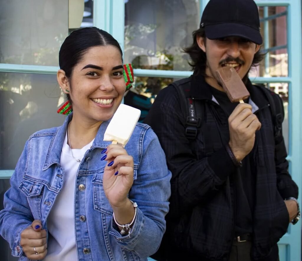 hombre y mujer comiendo paletas de helado en la entrada de la heladería