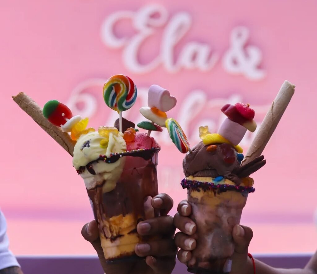 dos manos chocando vasos de helado con fondo de logo de ela & paleta