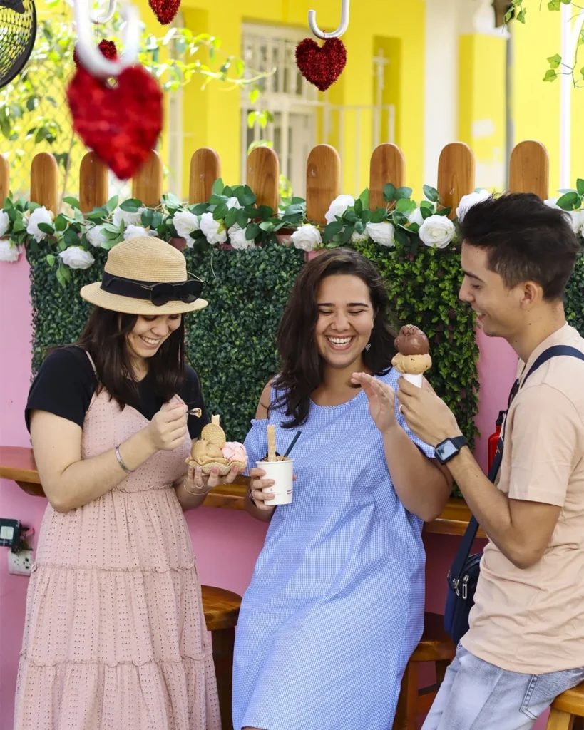 dos mujeres y un hombre comiendo helado en la entrada de la heladería